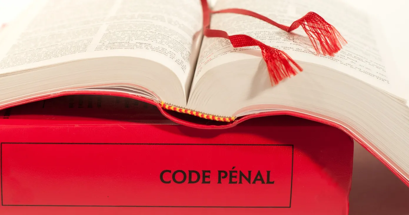 Un code pénal ouvert, signets rouges apparents, posé sur un second volume dont le dos porte la mention « Code pénal ».